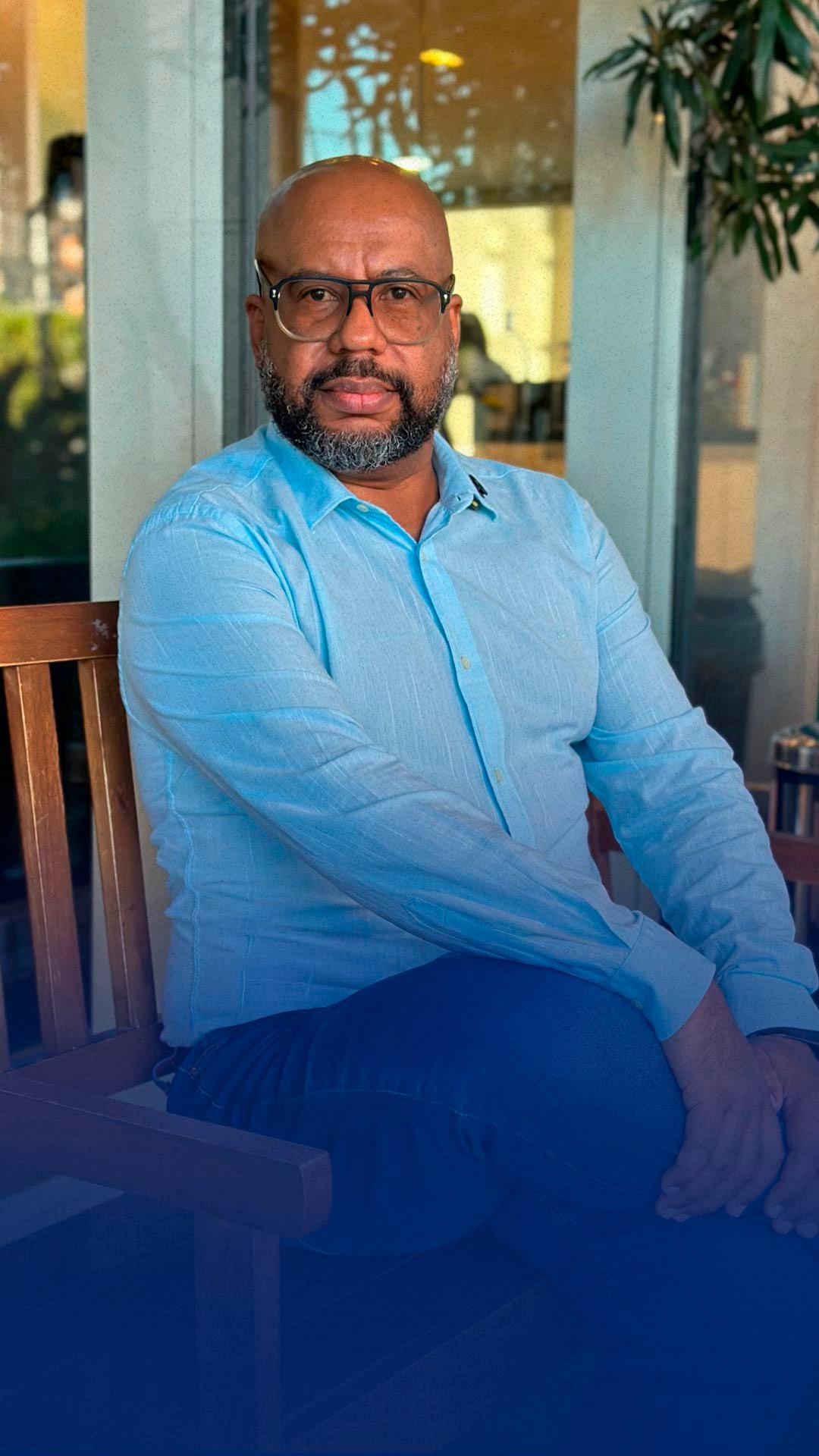 Rodrigo Lúcio vestindo roupas informais, sentado na varanda envidraçada de uma casa em um dia ensolarado.